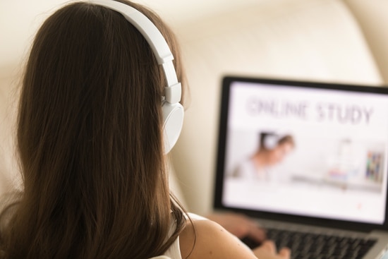 Woman in headphones sitting on sofa with laptop on knees studying online